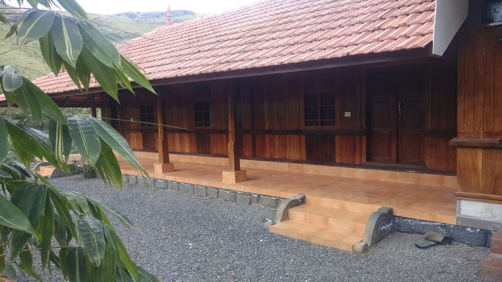 Traditional wooden cottage architecture with sloping tiled roof and veranda at Vagamon Bamboo Nest Resort