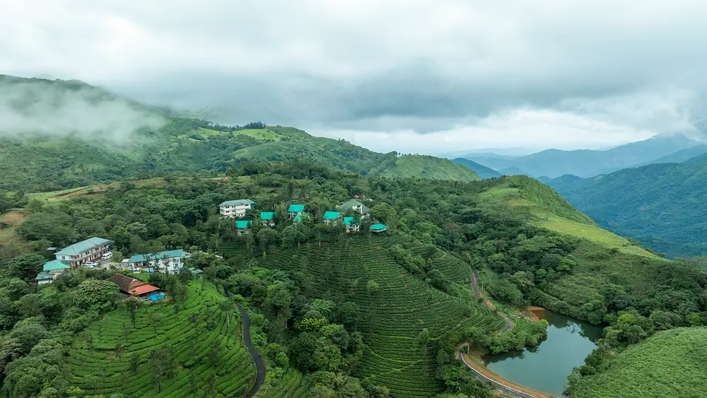 Aerial panoramic view of Winter Vale Green Stay surrounded by green hills and mist in Vazhikkadavu Vagamon