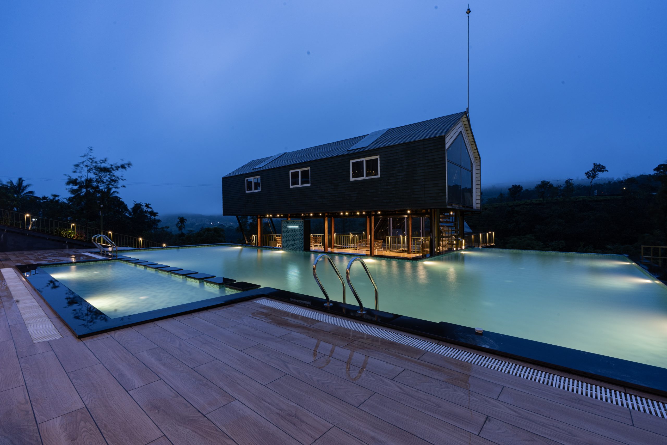 Santuario Resort illuminated swimming pool at dusk surrounded by modern accommodation buildings in Vagamon