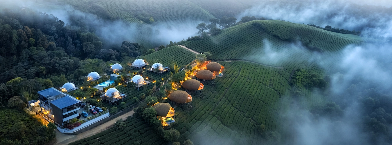 Aerial panoramic view of white luxury glamping domes scattered across misty green hills at Monticle Glamps Vagamon
