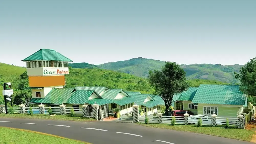 Scenic road view of Green Palace Residency cottages set against rolling green hills in Kolahalamedu Vagamon