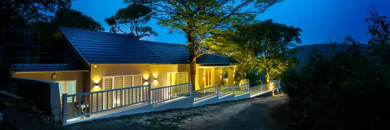 Illuminated exterior view of Willow House Cottages against a deep twilight sky in Vagamon