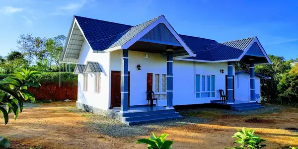 Exterior view of single story farmstay cottage with blue tile roof and courtyard at Thanal Farm Stay Vagamon