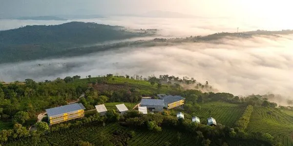 Panoramic aerial view of The Hosteller Bam Vagamon surrounded by misty green hills and valley clouds.
