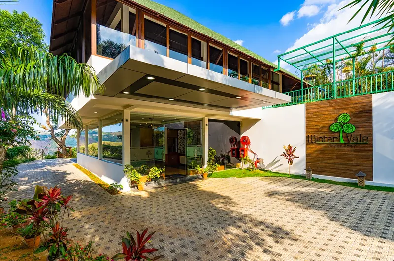Exterior view of modern resort building architecture and paved courtyard at Winter Vale Green Stay in Vagamon
