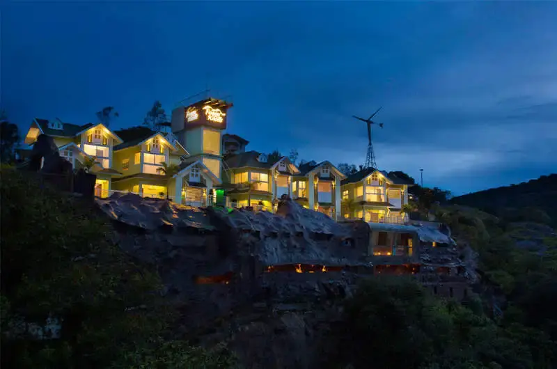 Illuminated hillside view of Foggy Knolls Resort cottages nestled among green mountains at night in Vagamon