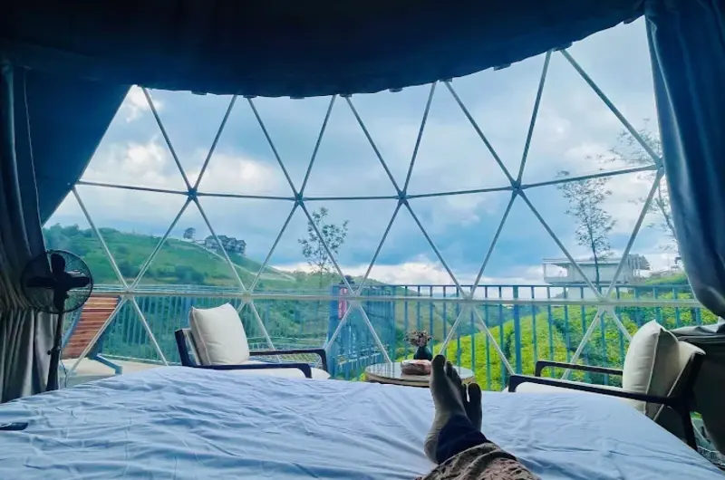 Interior view of a luxury glamping dome suite featuring a plush double bed, seating area, and panoramic window view
