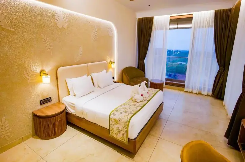 Comfortable guest bedroom with plush bedding, bedside lighting, and panoramic hill view window at Palette Hill View Resort