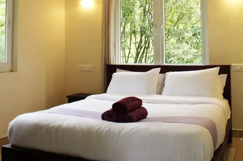 Cozy resort bedroom with comfortable double bed, clean white linens, and large window overlooking greenery
