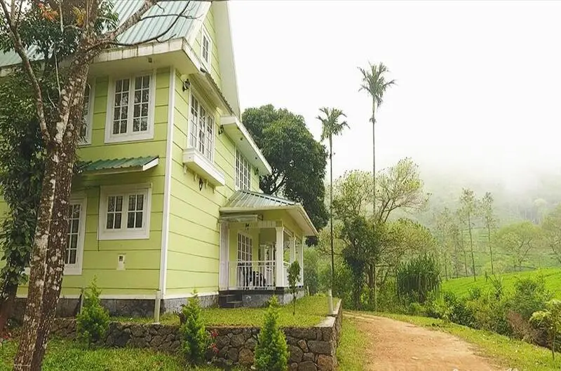 Side exterior view of multi-story green resort building surrounded by natural greenery in Vagamon