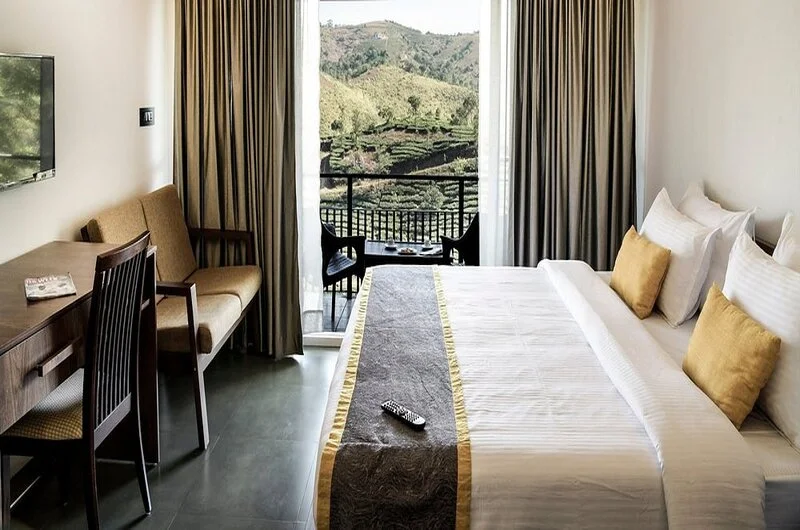 Spacious guest bedroom with multiple beds and private balcony window overlooking Vagamon hills at Falcon Crest Resort