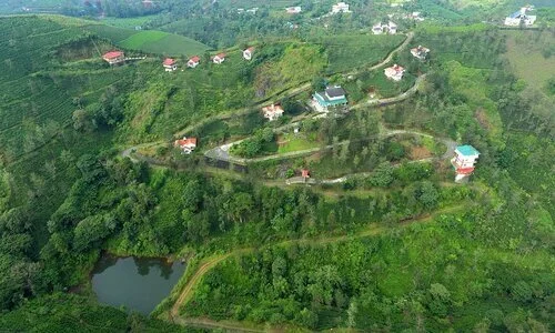Scenic hilltop view of Falcon Crest Resort surrounded by rolling tea estate hills and a natural pond in Vagamon