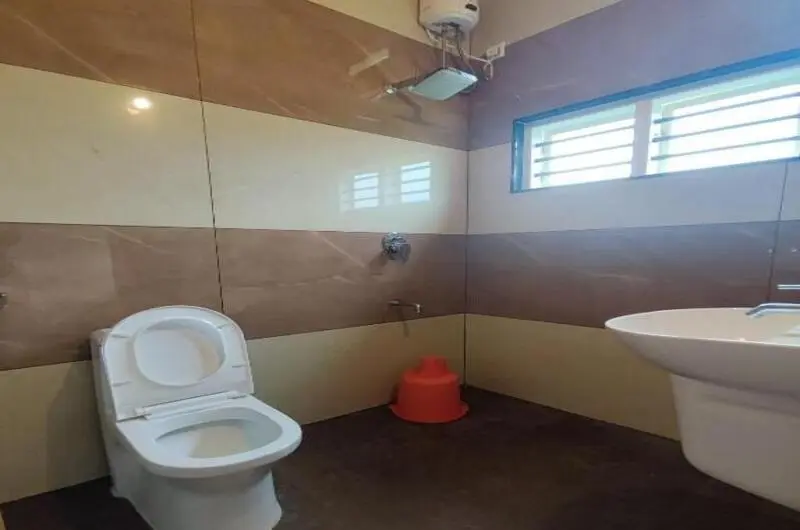 Clean attached bathroom with tiled walls, modern sanitary fixtures, and mirror at Green Palace Residency Vagamon