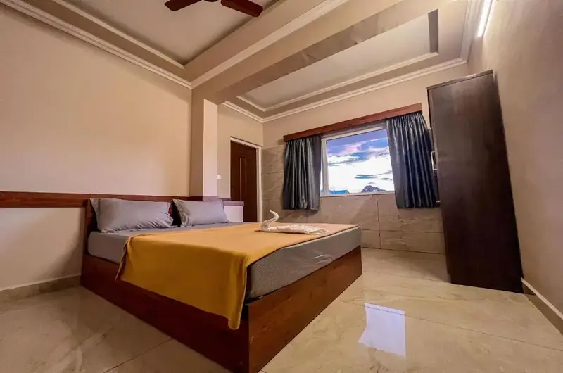 Spacious guest bedroom with plush double bed, warm ceiling lighting, and dark wood furniture at Green Palace Residency