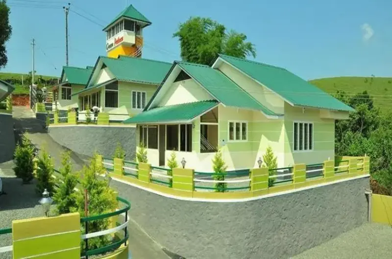 Front view of Green Palace Residency cottages featuring a manicured lawn and stone boundary wall in Vagamon