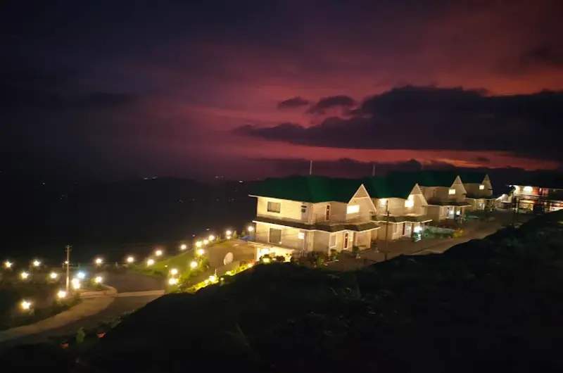 Illuminated night view of Orange Valley Hills Resort building against a clear evening sky in Vagamon
