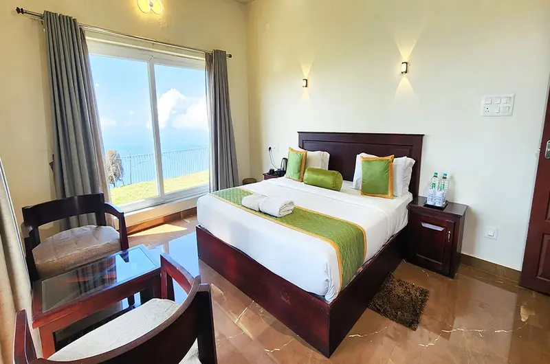 Comfortable guest bedroom with wooden flooring, premium bedding, and panoramic window view in Vagamon
