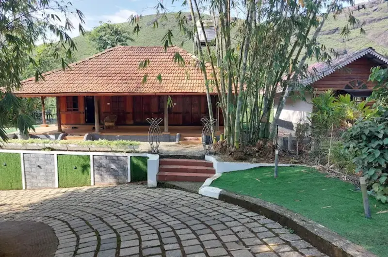 Traditional wooden bamboo cottage with sloping tiled roof set against green hills at Vagamon Bamboo Nest Resort