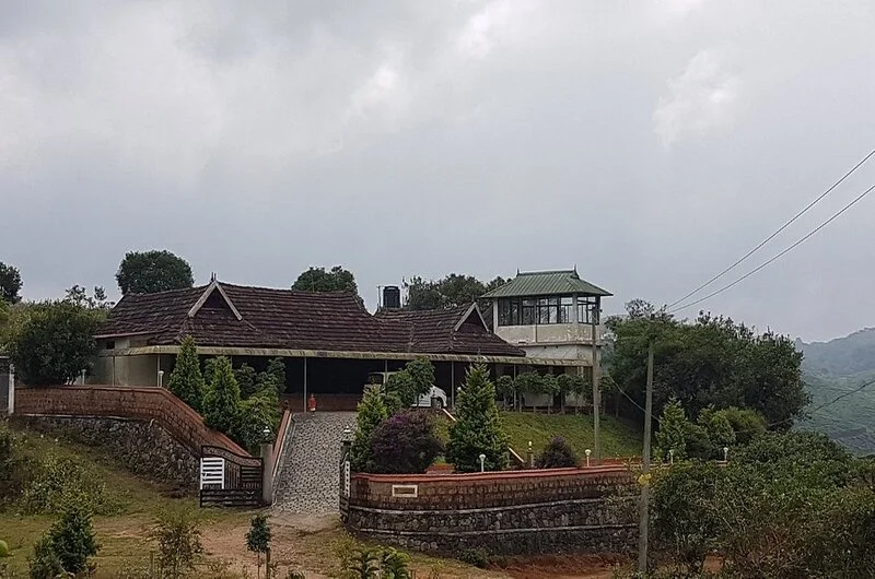 Exterior view of Wood Castle Residency set against green hills and mountain backdrop in Vagamon