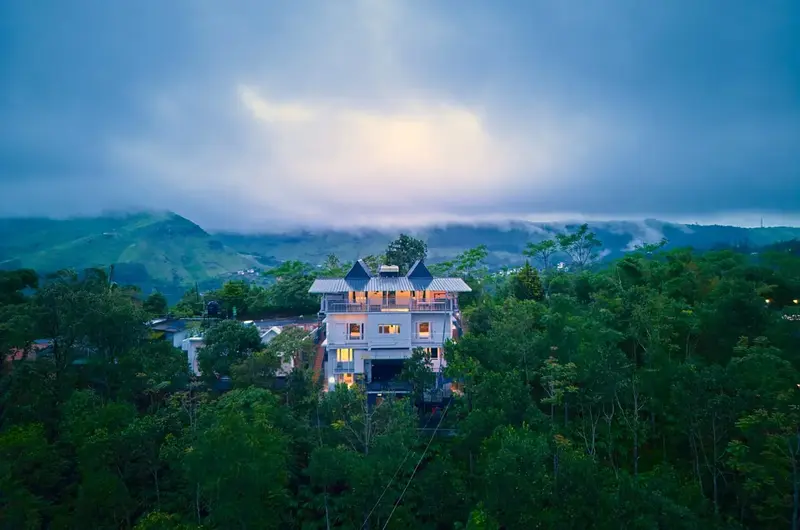 Distant view of Choice Holidays Resort Vagamon under a dramatic cloudy sky and mountain fog.