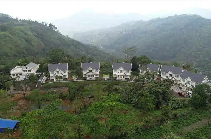 Hillside view of luxury white villas at The Grasmere Resort Vagamon under a misty sky.