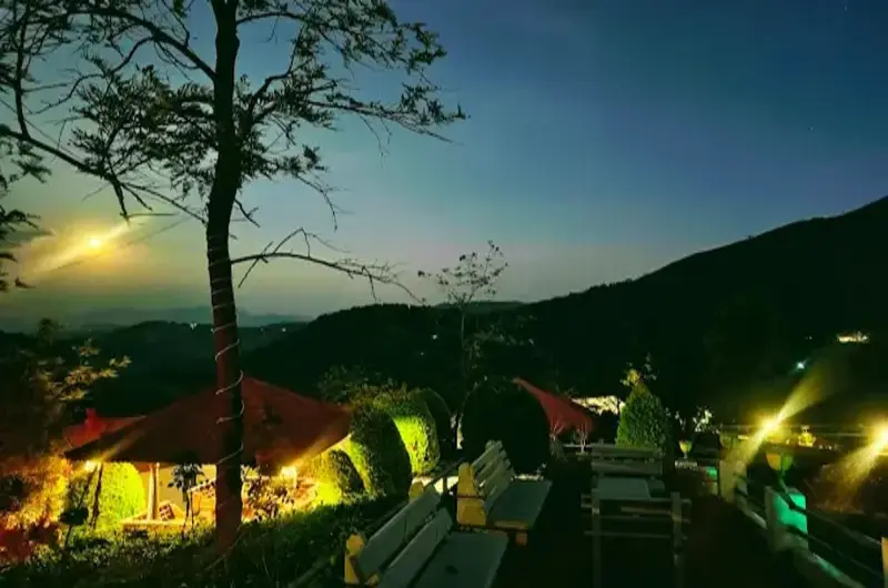 Night view of Heaven Valley Resorts Vagamon illuminated by warm lights amidst lush green trees and mountains.