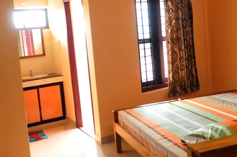 Comfortable homestay guest room with wooden bed frame and window overlooking Vagamon greenery