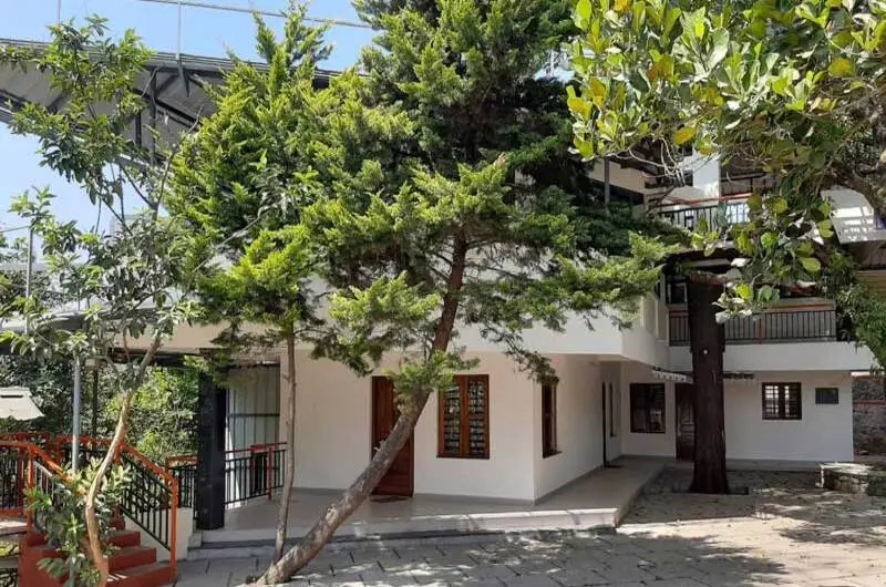 Exterior view of Padmalayam Homestay building with paved courtyard and surrounding garden trees in Vagamon