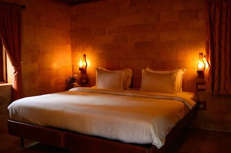 Rustic bedroom interior featuring earthen walls, warm lamp lighting, and comfortable bedding at SAJ Vagamon Hideout