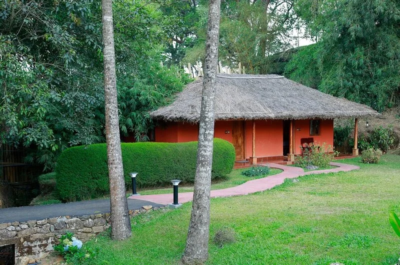Traditional eco-friendly cottage with thatched roof nestled on a lush green lawn at SAJ Vagamon Hideout