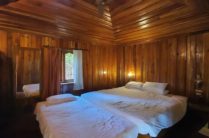 Spacious traditional mud cottage bedroom with twin beds and wooden ceiling architecture at SAJ Vagamon Hideout