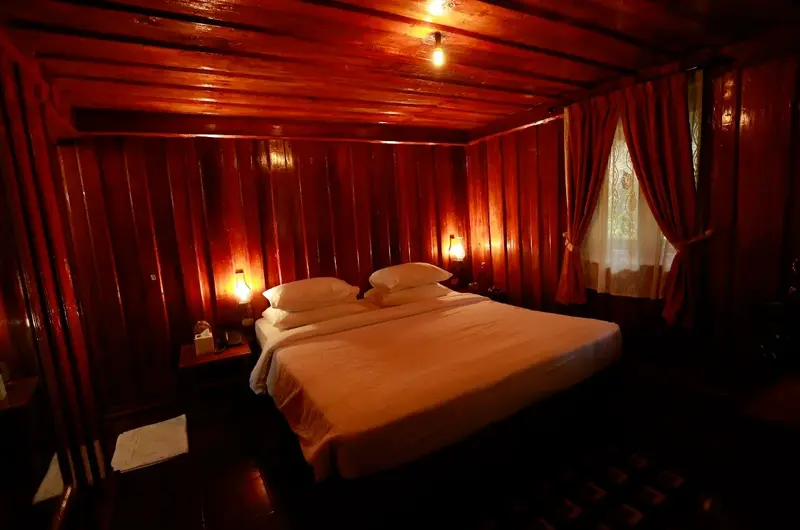 Cozy traditional cottage bedroom featuring a double bed, warm lamp lighting, and rich wood-paneled walls at SAJ Vagamon Hideout
