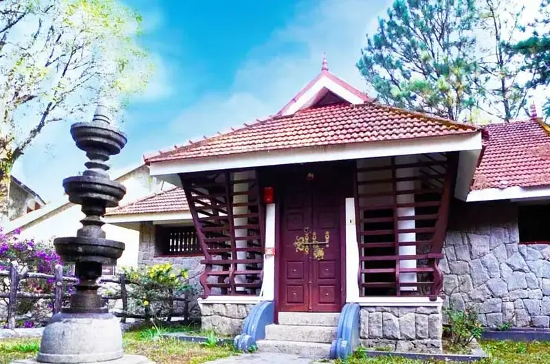 Traditional Kerala heritage cottage entrance featuring carved wooden doors and stone pillar at Adrak Summer Sand Hill Resort Vagamon