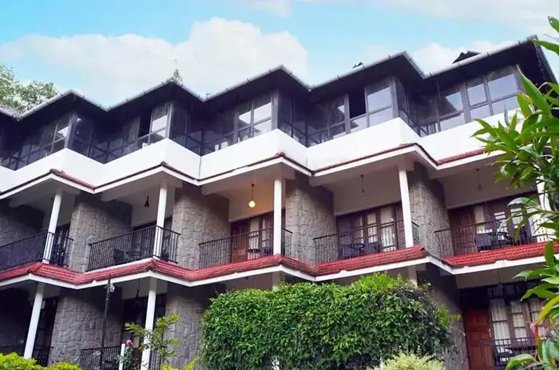 Multi-story resort accommodation building with stone and wood exterior facade surrounded by greenery at Adrak Summer Sand Hill Resort Vagamon