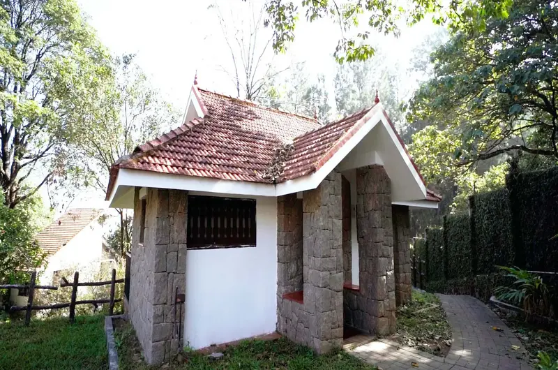 Exterior view of a stone cottage villa surrounded by lush garden trees at Adrak Summer Sand Hill Resort Vagamon
