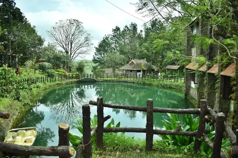 Lush hill view over a natural pond bordered by a wooden fence at Adrak Summer Sand Hill Resort Vagamon