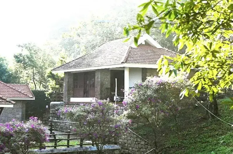 Scenic hill resort garden with manicured lawn, stone pathway, and cottage villas in Vagamon