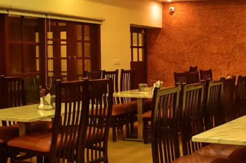 Warmly lit indoor resort restaurant dining room with dark wooden tables and chairs at Adrak Summer Sand Hill Resort