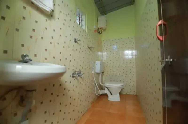 Clean attached guest bathroom featuring modern sanitaryware and tiled walls at Himaharsham Homestay