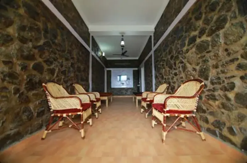 Covered verandah corridor featuring stone walls and wicker patio chairs at Himaharsham Homestay
