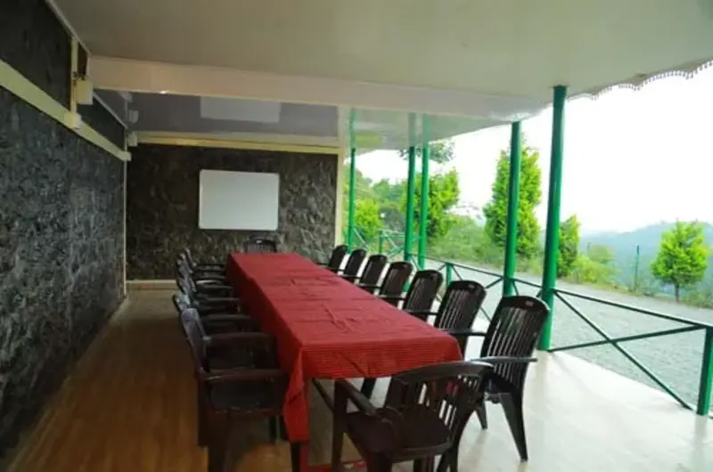 Outdoor balcony dining area with long table setup and scenic hill views at Himaharsham Homestay