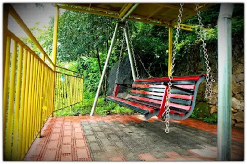 Covered porch balcony featuring a traditional red swing chair overlooking garden greenery