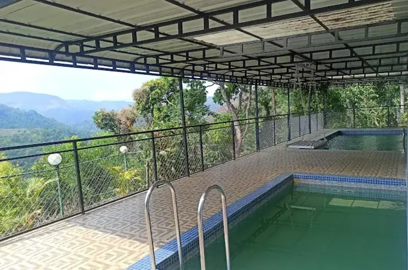 Covered outdoor swimming pool overlooking lush green mountain valleys at Theeram Agro Farm Hill Resort