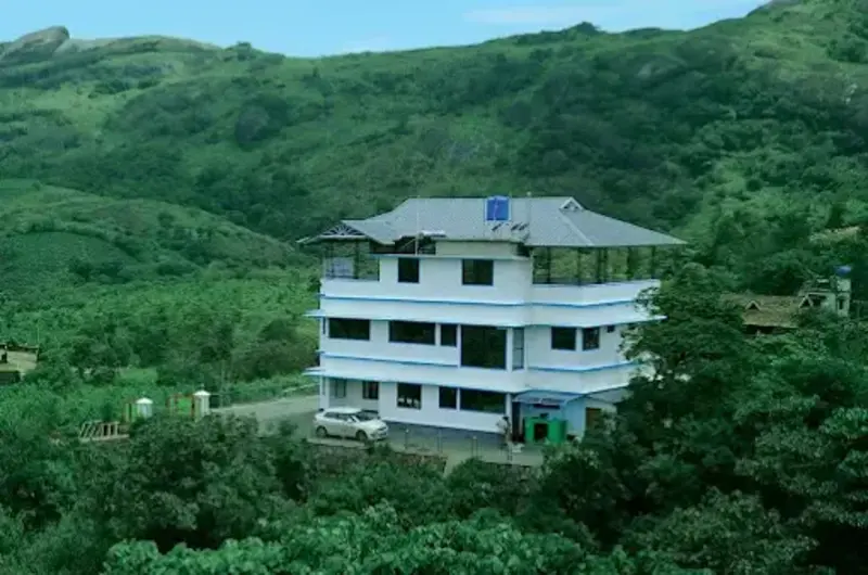 Exterior view of Snow White Residency hotel building surrounded by green mountain hills in Vagamon