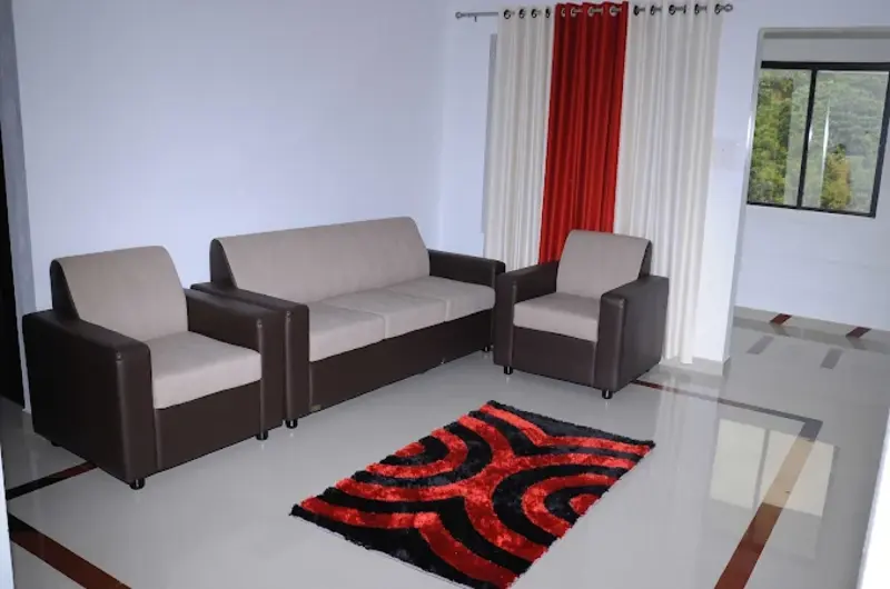 Spacious suite lounge area featuring modern couch seating, red pattern rug, and full-length windows