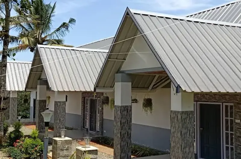 Exterior view of modern villa cottages featuring slanted metal roofs and stone accent pillars in Peerumade