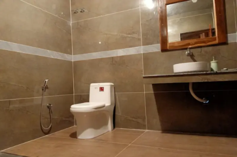 Clean attached guest bathroom featuring modern tiled walls, mirror, and sanitary fittings