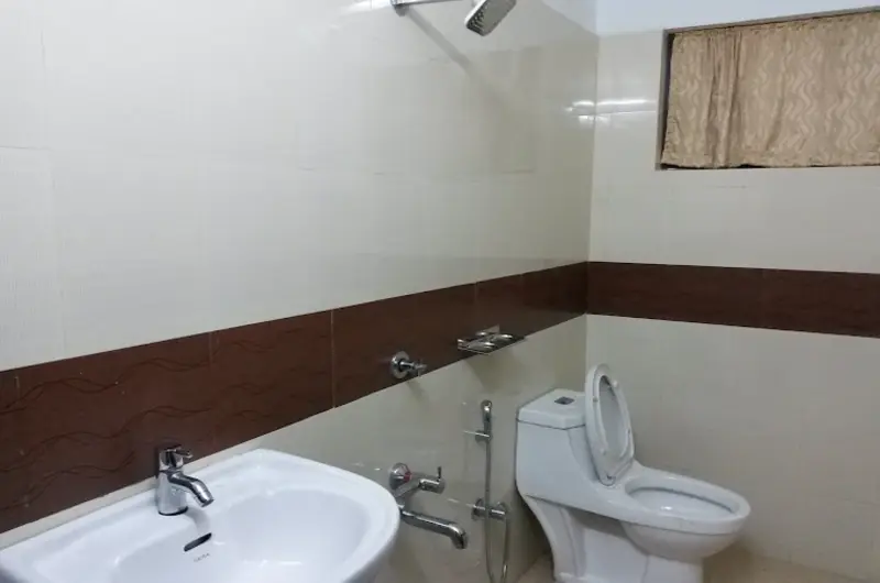 Modern attached guest bathroom with tiled walls, ceramic washbasin, and western toilet