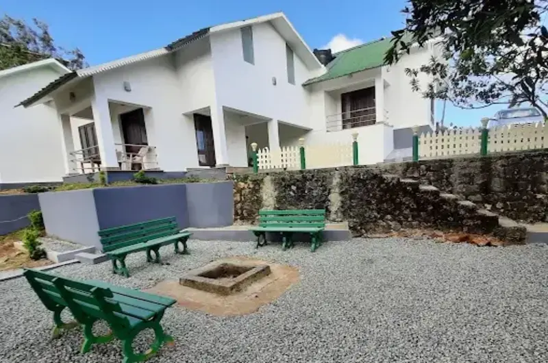 Exterior view of white cottage building with green roof trim at Pine View Homestay Vagamon