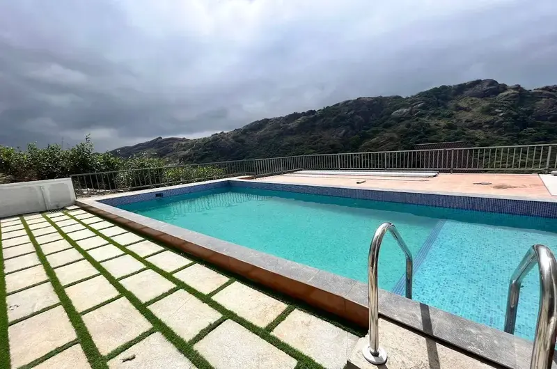 Outdoor swimming pool with tiled sun deck overlooking green hill views at JMount Vagamon Resort